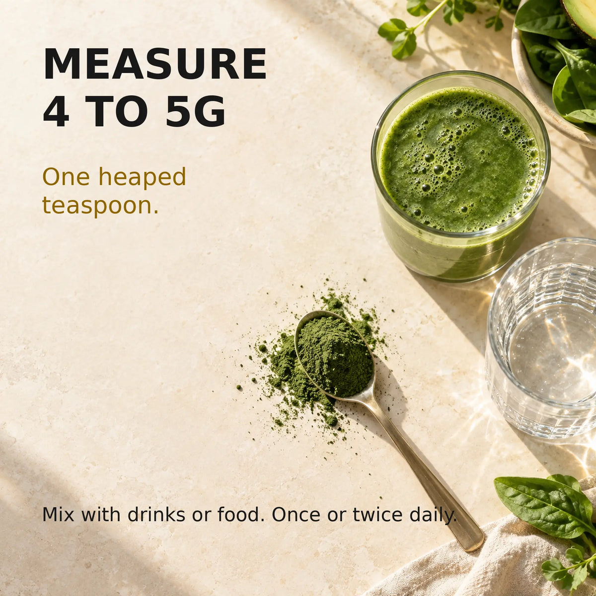 A heaped teaspoon containing 4 to 5g of green powder beside water and a green smoothie, illustrating suggested use.