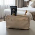 Beige toiletry bag with a Ormus Fluoride free Botanical Toothpaste tube and wooden toothbrush on a table.