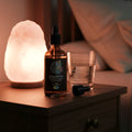 Bottle of 'Lucid Dreaming' tincture on a nightstand with a salt lamp and glass.