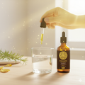 Hand holding a dropper with a glass of water and a bottle labeled 'Solar Plexus Chakra' on a light surface.