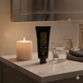 Tube of 'Ormus Fluoride free Botanical Toothpaste' product on a bathroom counter with a candle and glass.