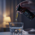 Hand dropping liquid from a dropper into a glass with a blurred background