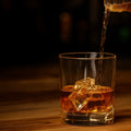 Gold being poured into a glass with ice cubes on a wooden surface.