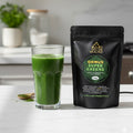 Glass of green juice next to a package of Gold Healing ORMUS Super Greens on a kitchen counter.