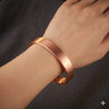Copper magnetic bracelet on a wrist against a dark background