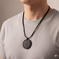 Person wearing a necklace with a dark pendant on a plain background