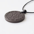 Round pendant with intricate design on a black cord against a white background
