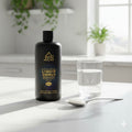 Bottle of GoldHealing Liquid Ormus on a table with a glass of water and spoon.