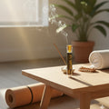 Incense stick with smoke on a wooden table, with a yoga mat and plant in the background.